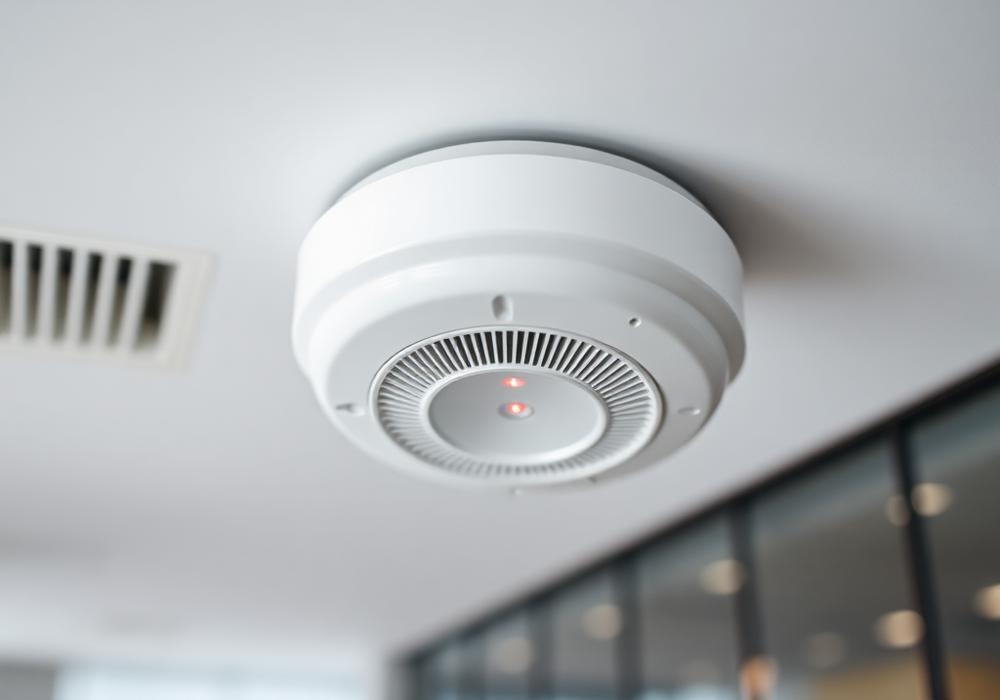 Smoke detector optik terpasang di plafon kantor modern dengan indikator LED merah